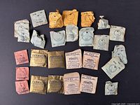 Photo of approximately 30 small paper envelopes containing vintage new old stock pocket watch crystals in various sizes and different colored packaging.