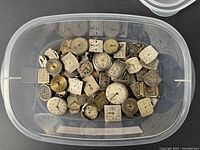 Plastic container filled with various vintage men's watch movements and dials, mostly square and round faces showing wear and dirt accumulation