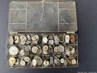 Plastic box with 30 compartments holding various vintage women's watch movements and dials, showing different sizes and visible wear
