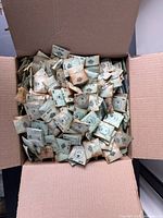 Cardboard box filled with over 1000 small sealed paper envelopes of watch crystals