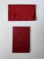 Closed red suede pouch and Cartier booklet placed underneath, showing front of both items