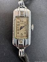 Full view of the vintage Swiss made ladies Lorie wristwatch with rectangular face and black fabric strap.