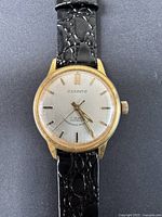 Close-up of watch face showing time, gold-tone hands, and textured black strap attached.