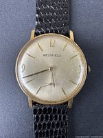 Front view of the vintage Westfield wristwatch showing the gold-tone case, white dial with gold numerals and markers, and black leather strap.