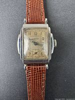 Full front view of vintage rectangular men's wristwatch with aged dial and brown leather strap.