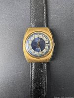 Front angle of vintage Briran watch case and black leather strap on black background.