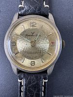 Front view of vintage Hamilton men's watch showing silver-tone textured dial with Arabic numerals and black leather strap with white stitching.