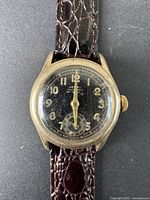 Close-up front view showing black dial, gold-tone case, Arabic numerals, and subdial at 6 o'clock with wear and scratches.