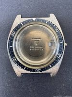 Front view of watch case with bezel and crystal intact showing model number and Swiss markings inside crystal.