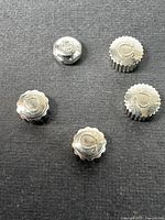 Five vintage stainless steel watch crowns arranged on a black background showing their tops with a C logo