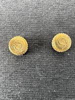 Two vintage brass watch crowns with embossed 'S' logos on dark textured background, shows age and wear.