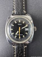 Close-up view of the watch face showing the Timex brand, black dial, date window at 3 o'clock, orange second hand, and worn condition.