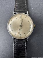 Front view of vintage Timex men's watch showing silver-tone dial with black markers and hands, reading 'Timex' and 'Waterproof'. Black leather strap visible.