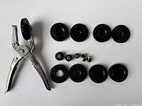 Photo showing the vintage metal watch crystal press hand tool and eleven black round dies in various sizes laid out on a flat surface.