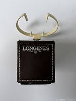 Photo of Longines watch dealer display stand showing the leather wrapped base with stitched edges and Longines logo, topped with a cream-colored plastic watch holder.