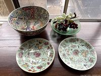 Overview of lot showing large porcelain bowl, two decorative plates, green glass bowl with stone grapes
