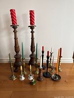 Front view showing all candlesticks arranged on floor with various candles including tall wooden candlesticks, brass, ceramic holders and small decorative ceramic flower holder.