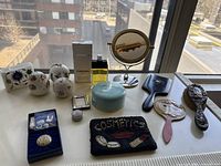 Overview of all items on windowsill including perfume, box, mirrors, brushes, trinket boxes, pouch and enamel buttons