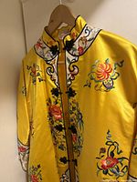 Front close-up of the yellow robe showing embroidered floral designs and black frog closures along the front.