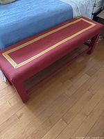 Red and gold fabric long narrow bench shown from an angle next to a bed, illustrating length and design.