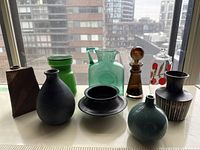 Nine vases and containers displayed on a windowsill against an urban backdrop