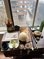 Full assortment on wooden table by window including vase, tin box, trinket dishes, egg, marquetry plaque and assorted small objects