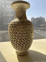 Front view of off-white openwork porcelain vase showing pierced geometric lattice pattern and flared rim.