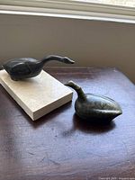 Two carved stone geese sculptures pictured on a dark surface, one on a marble base showing size and detail.