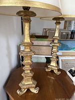 Close-up of two gilt wood table lamps showing carved stepped bases and curled feet.