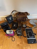 Overview of lot showing camera bags, cases, binoculars, digital camera, exposure meter, Bell & Howell viewer, Polaroid film back and flash reflector unit