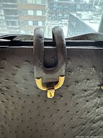 Close up image of the U-shaped gold-tone clasp on black ostrich leather handbag showing texture and clasp detail.