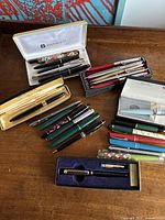 Overview of multiple pens in boxes and loose on table showing Parker, Sheaffer, Aurora, P. Penizzo and assorted pens