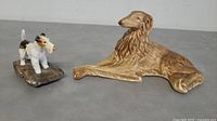 Photo of two dog sculptures side by side on a dark surface showing the Sylvac Borzoi lying and Wire Fox Terrier on a base