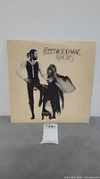 Front cover of Fleetwood Mac Rumours LP album showing two band members posing on a cream background with title.