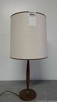 Full view of the Mid-Century Modern style table lamp showing the wooden base and beige fabric lampshade with brown trim.
