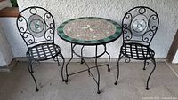 Full set showing one round table and two matching metal chairs with mosaic tile insets on the backs and tiled tabletop.