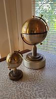 Two brass globes on round stands; larger globe is 8 inches, smaller is 4 inches and functions as a lighter.