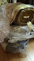Three plastic-wrapped bolts of vintage drapery fabric stacked on hardwood floor