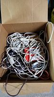 Top-down view of tangled electrical cords inside a cardboard box