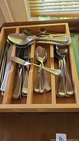 Overall view of cutlery set organized in a wooden drawer organizer showing spoons, forks, knives, and butter spreader
