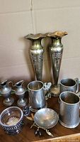 Mix of metalware items including two tall vases, lion handled pewter mug, small pitchers, squirrel bowl, hammered tankard and stainless steel/brass bases