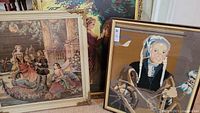 Three framed needlepoint pictures leaning against a wall showing various scenes, including a woman spinning and a group of historical figures outdoors.