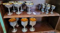 Six champagne cups, six red wine goblets, and six sherry glasses displayed on wooden shelving.