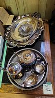 Top view showing two silver plated trays and a decorative silver bowl on one tray, with coffee and tea pots and other items on the other tray.