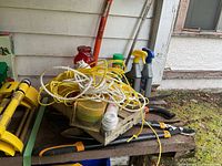 Yellow and white ropes, gardening sprays, and holders arranged on wooden surface outdoors.