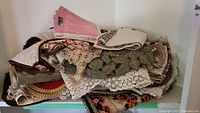 Pile of assorted vintage table linens including lace runners, small tablecloths, and printed fabric pieces