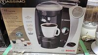 Photo of boxed Tassimo T45 Suprema coffee maker by Bosch with branding and product information visible, emphasizing new condition and untested status.