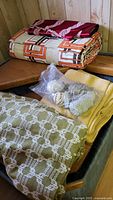 Multiple upholstery fabric bolts and trim bag on wooden surfaces showing patterns and folds.