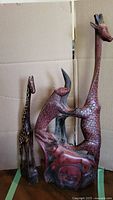 Front view of two red wood animal carvings, one tall giraffe, one large multi-animal carving base with giraffe and leopard