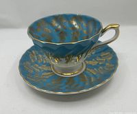 oblique view of teacup resting on saucer showing blue glaze and gold leaf pattern